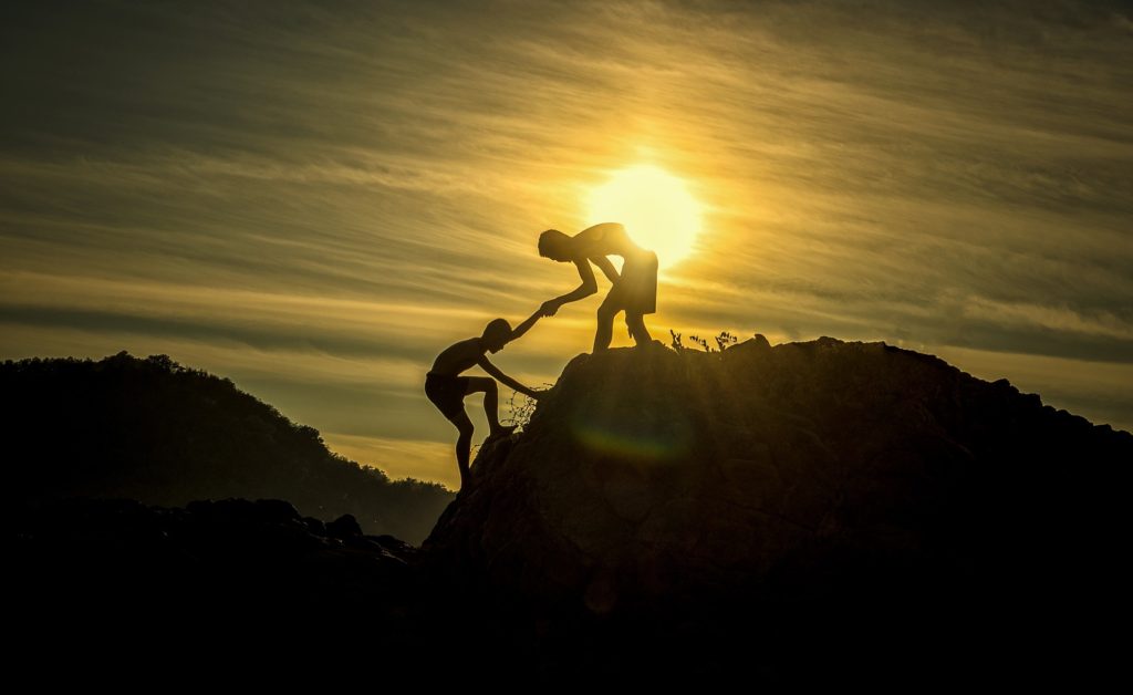 person helping another person on top of a rock
